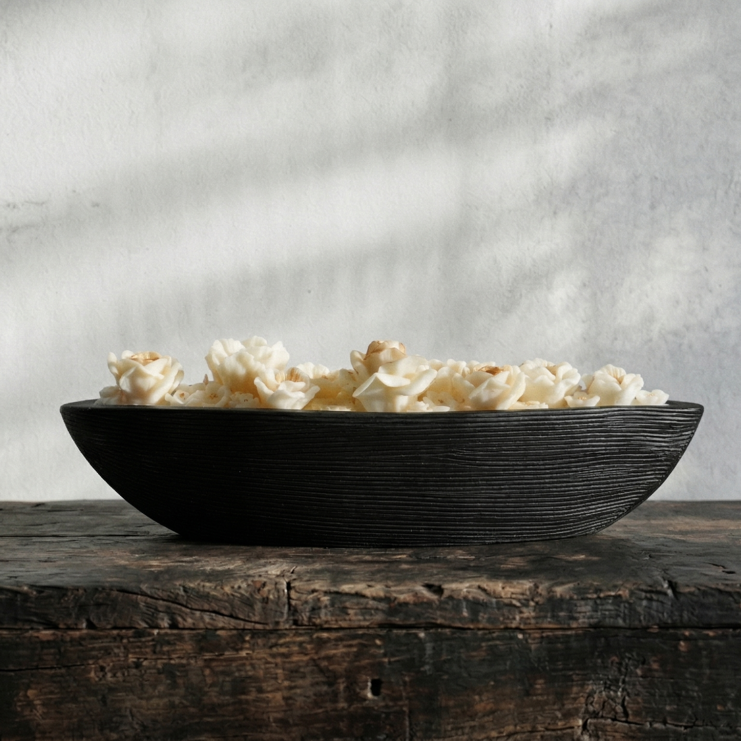 Black bowl filled with popcorn on a wooden surface with a gray textured background