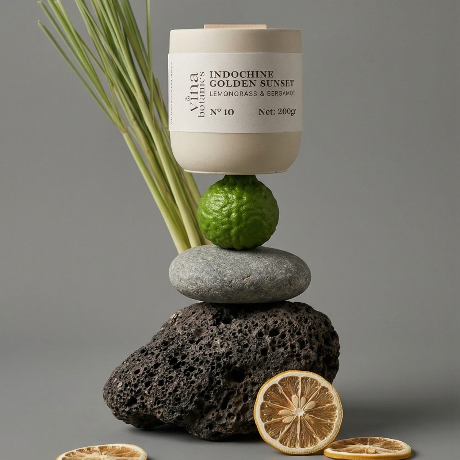 Candle labeled 'Indochine Golden Sunset' on stones with lemongrass, lime, and dried citrus slices.