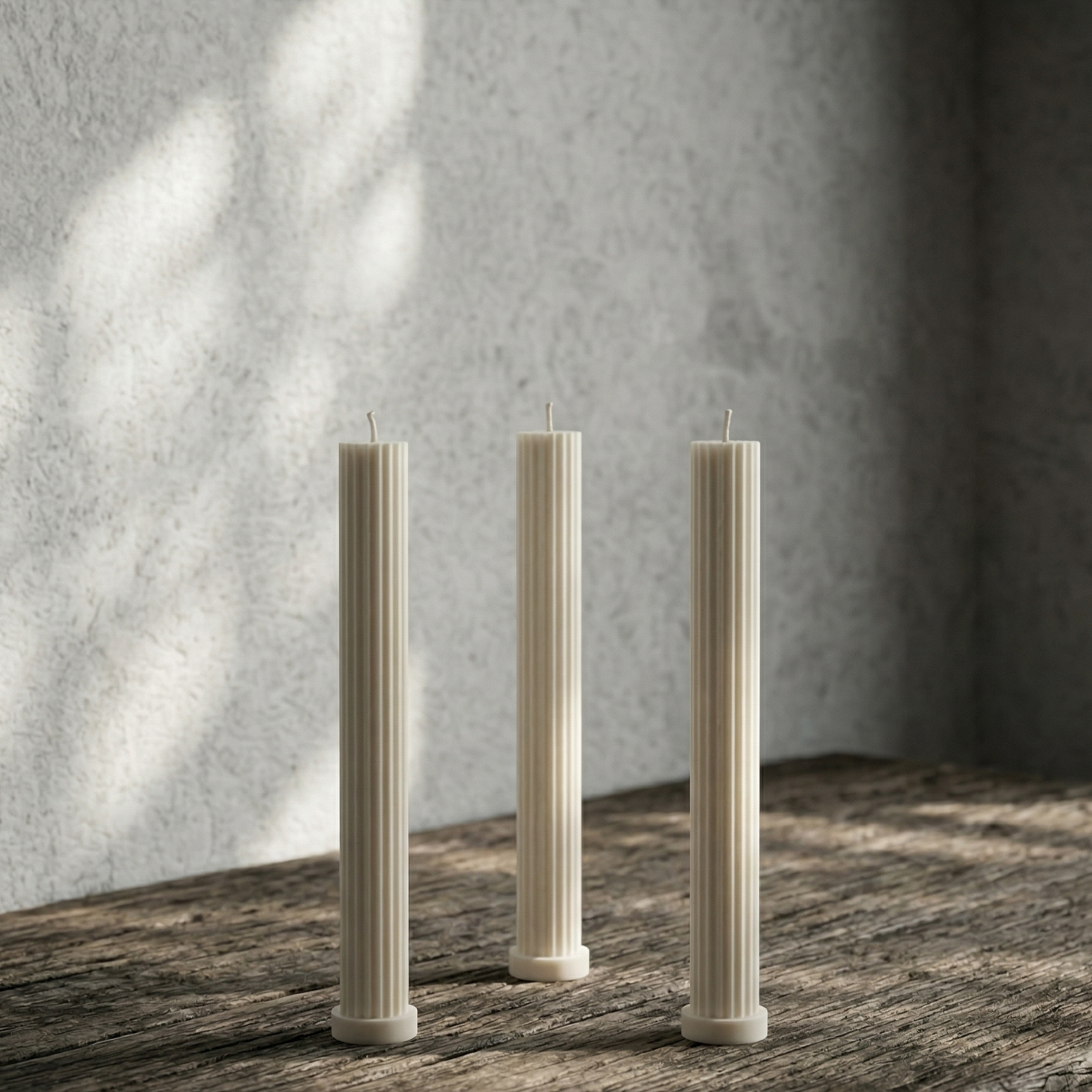 Three tall, thin candles on a wooden surface with a textured wall background