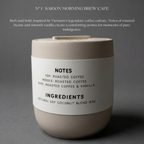 Candle with a label on a gray background, featuring details about the candle's notes and ingredients.